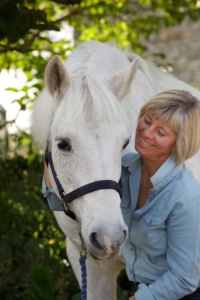 Image of Rosie Withey, Emotional Wellbeing Coach on the right, with a white horse on the left. They are holding their faces close together and both look happy