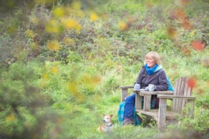 portrait of rosie sitting on a wooden seat with a jack russel dog at her feet and a pen in her hand