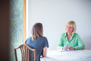 A photo of Rosie helping a client during a 121 therapy session.Rosie is facing the camera and is wearing a green blouse. The client has her back to the camera and is wearing a blue tshirt.